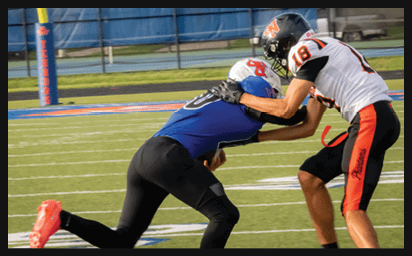 Two people in football uniforms are engaged in a tackle on a grassy field near the end zone. Description generated by AI