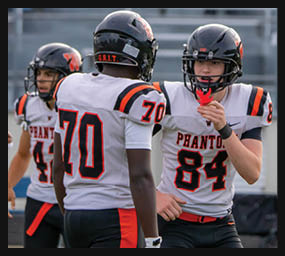 Three people wearing football uniforms with helmets are on a field, with one person holding a red object near their mouth. Description generated by AI