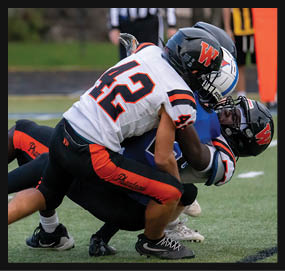 Two football players in helmets and uniforms are engaged in a tackle on a grassy field during a game. Description generated by AI