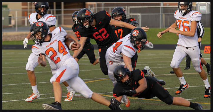 Adults in football uniforms are actively playing on a field with some players in black uniforms tackling or chasing others in white uniforms. Description generated by AI