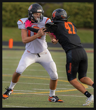 Two people in football uniforms are engaged in a play on a field, with one person in white and the other in black and orange, the person in black pushing against the person in white. Description generated by AI