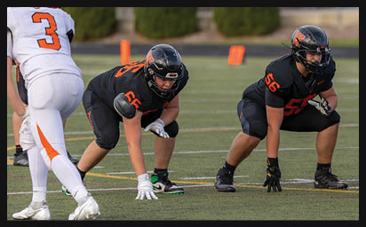 Two people in black football uniforms are crouched in a ready position on a field facing a person in a white football uniform with the number 3. Description generated by AI