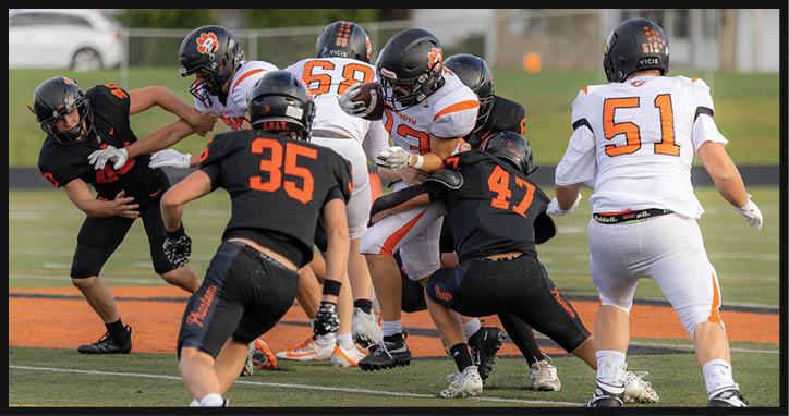 Several people wearing football uniforms are engaged in a play on a field with some players in black and orange and others in white and orange. Description generated by AI