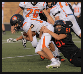 A person in a black football uniform with the number 91 is tackling another person in a white football uniform with orange accents during a game. Description generated by AI
