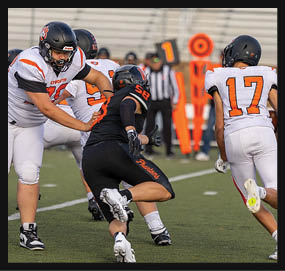 Four people in football uniforms are actively playing on a field with one person in black running while others in white attempt to block or catch. Description generated by AI