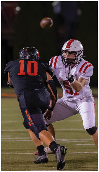A person in a white football uniform with red stripes is reaching out to catch a football while facing an opponent in a black uniform on a football field at night. Description generated by AI