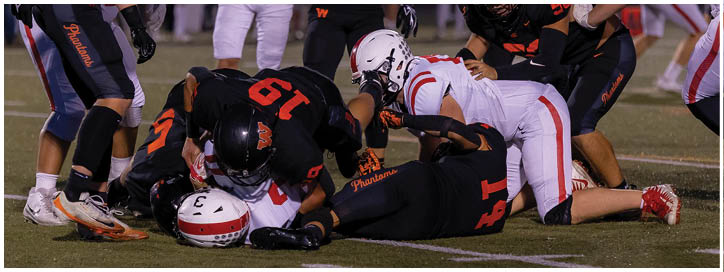 People wearing football uniforms are engaged in a play on a field, with some players standing and others on the ground. Description generated by AI