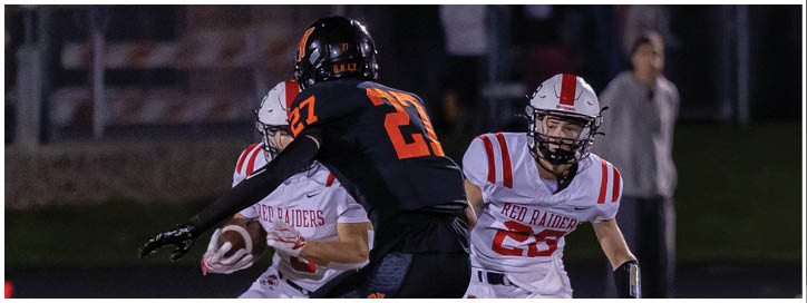Two people in football uniforms are engaged in a play on a field at night, with one person holding the ball and the other preparing to block or tackle. Description generated by AI