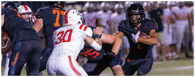 A person in a black football uniform is running with the ball while being tackled by a person in a white football uniform on a field. Description generated by AI