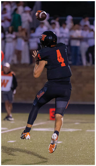 A person wearing a dark sports uniform with the number 4 is throwing a football on a field with spectators in the background. Description generated by AI