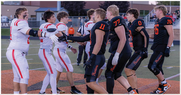 People wearing football uniforms in black and white are shaking hands on a field after a game. Description generated by AI