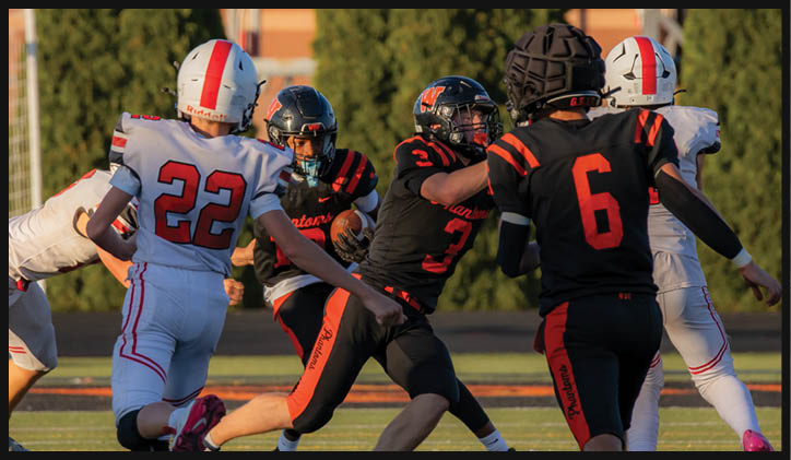 People wearing football uniforms are actively engaged in a play on a grassy field during a game. Description generated by AI