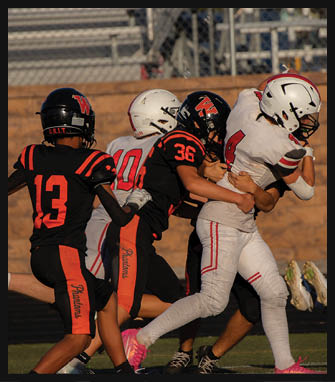 Four people wearing football uniforms are engaged in a play on a field with two players in black and orange uniforms tackling two players in white uniforms. Description generated by AI