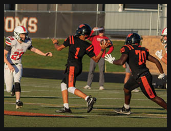 Two people in black and orange football uniforms are on a field with one preparing to throw a football to the other. Description generated by AI