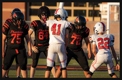 Five people wearing football uniforms are standing on a field facing each other, with two in white uniforms and three in black uniforms. Description generated by AI