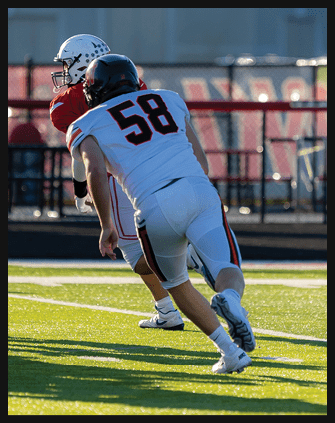 A person wearing a black helmet and a white sports jersey with the number 58 is seen from behind against a blurred outdoor background. Description generated by AI