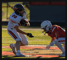 A person wearing a white football uniform with the number 20 is running on a field while holding a football and facing another person in a white helmet. Description generated by AI