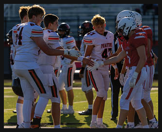 Players from two opposing football teams in uniforms and helmets are shaking hands on a field at sunset. Description generated by AI