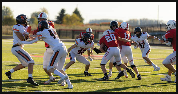 People wearing helmets and sports uniforms are actively engaged in a football game on a grassy field. Description generated by AI