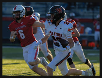 A person in a white football uniform with a black helmet is running with the ball while being chased by a person in a red football uniform on a sunlit field. Description generated by AI