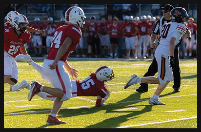 A group of people in football uniforms are on a field with one person diving toward the ground while others run nearby during a game. Description generated by AI