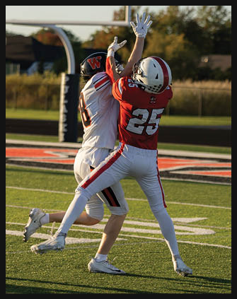 Two people in football uniforms are competing to catch a football near the end zone on a sunlit field. Description generated by AI