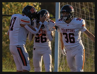 Three people in football uniforms stand on a field with one person comforting another while the third person gestures with an arm extended. Description generated by AI