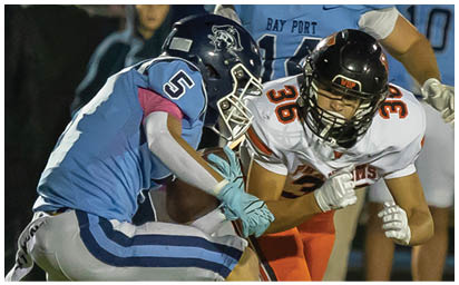 Two people in football uniforms are engaged in a play on the field with one wearing a light blue jersey and the other wearing a white jersey with orange and black accents. Description generated by AI