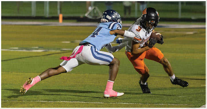 A person in orange sportswear is running with a football while another person in blue sportswear is attempting to tackle them on a grassy field. Description generated by AI