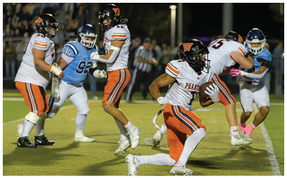 A person in a white and orange football uniform is running with the ball while several other players in blue and white uniforms and white and orange uniforms are on the field during a game. Description generated by AI