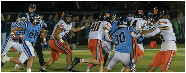 People wearing football uniforms are actively playing on a field under stadium lights during a nighttime game. Description generated by AI