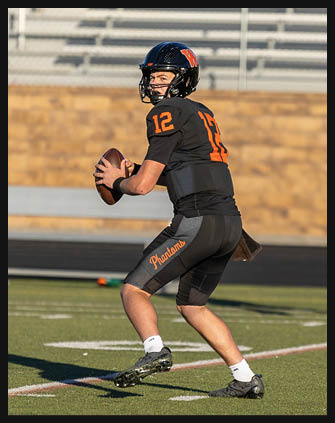 A person wearing black athletic shorts and cleats is running or preparing to move on a green sports field with white yard lines. Description generated by AI