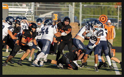 Players in dark and white football uniforms are engaged in a play on a grassy field with a chain marker showing the number three in the background. Description generated by AI