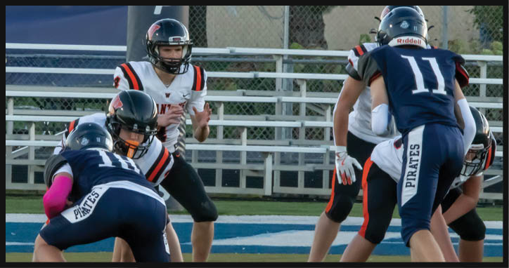 Adults in football uniforms are engaged in a play on a field with bleachers and a goalpost in the background. Description generated by AI