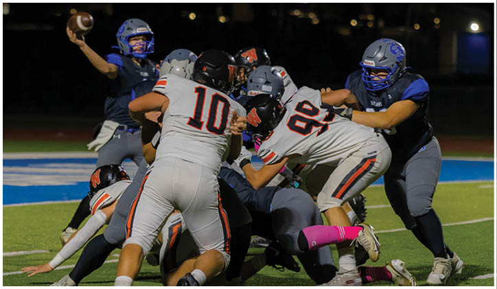 Several people in football uniforms are engaged in a close, intense play on a field at night. Description generated by AI