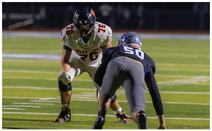 Two people in football uniforms are positioned facing each other on a field, preparing for a play. Description generated by AI