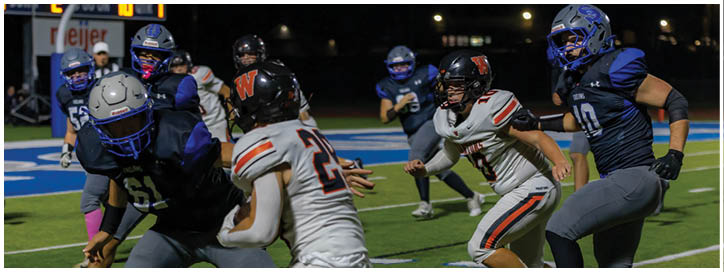 People in football uniforms are actively engaged in a game on a field under stadium lights. Description generated by AI