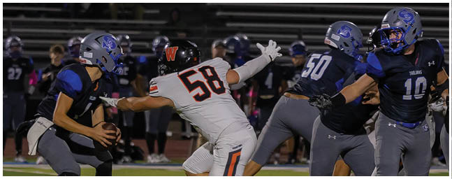 People in football uniforms are actively engaged in a play on a field, with one person holding the ball and others attempting to block or tackle. Description generated by AI
