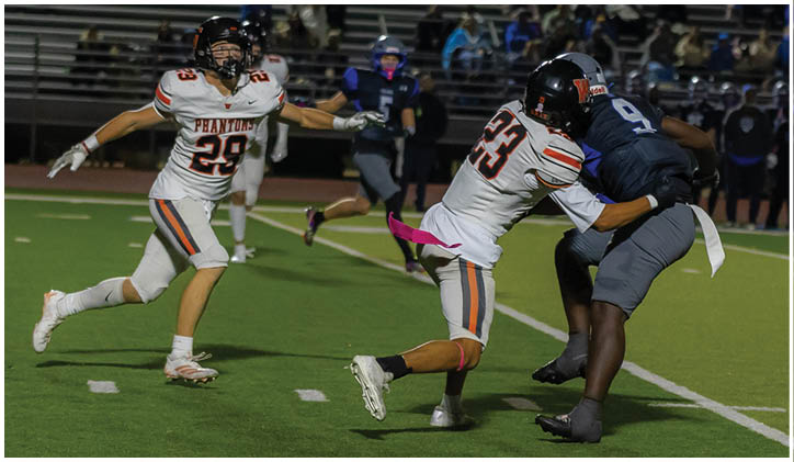 Two people in white sports uniforms are attempting to tackle a person in a dark sports uniform on a football field during a game. Description generated by AI