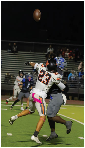 Two people in football uniforms are jumping and reaching for a football in midair on a field with spectators in the background. Description generated by AI