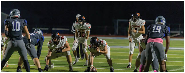 People in football uniforms are lined up on a field at night preparing for a play. Description generated by AI