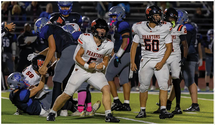 People in football uniforms are engaged in a game on a field with one person on the ground and others standing or crouching nearby. Description generated by AI