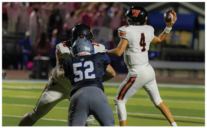 Three people in football uniforms are on a field with one person preparing to throw a football while two others engage in blocking or tackling. Description generated by AI