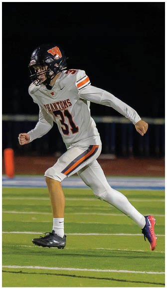 A person wearing a white football uniform with the number 31 and a black helmet is running on a football field at night. Description generated by AI