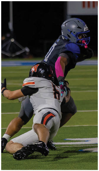 Two people in football uniforms are engaged in a tackle on a grassy field during a nighttime game. Description generated by AI