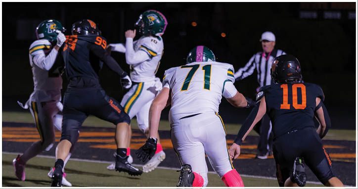 Two people in football uniforms are running on a field with a referee in the background. Description generated by AI