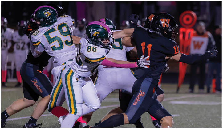 Several people in football uniforms are actively engaged in a play on a field under stadium lights. Description generated by AI