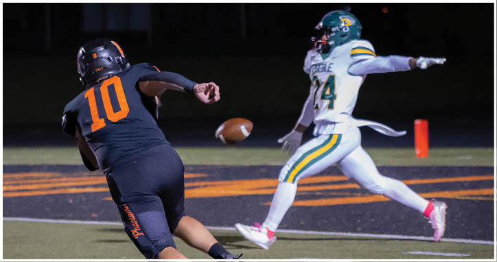 A person in a black sports uniform with the number 10 is running on a football field while another person in a white and green uniform with the number 14 is reaching out toward a football in midair near the end zone. Description generated by AI