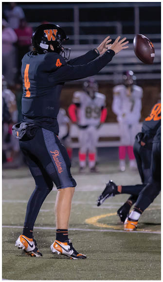 A person wearing a dark sports uniform with the number 4 and the word “Phantoms" on the pants is preparing to throw a football on a field during a game. Description generated by AI