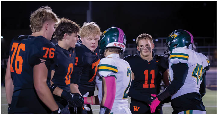 A group of people wearing football uniforms are gathered on a field at night, with some smiling and interacting. Description generated by AI